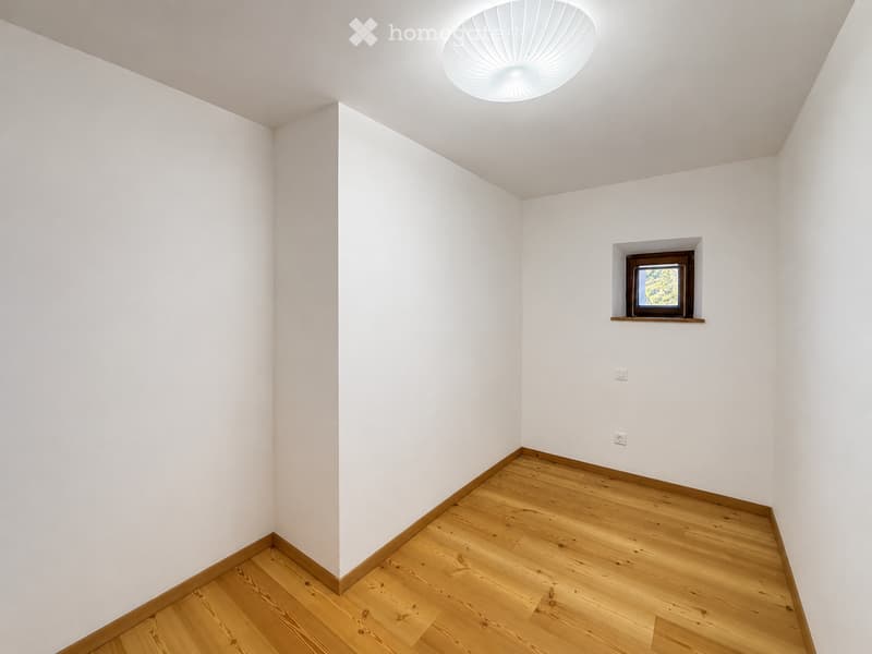 Empty room with white walls, wooden floor, and a single built-in shelf holding a framed picture. The ceiling features a modern, round light fixture.