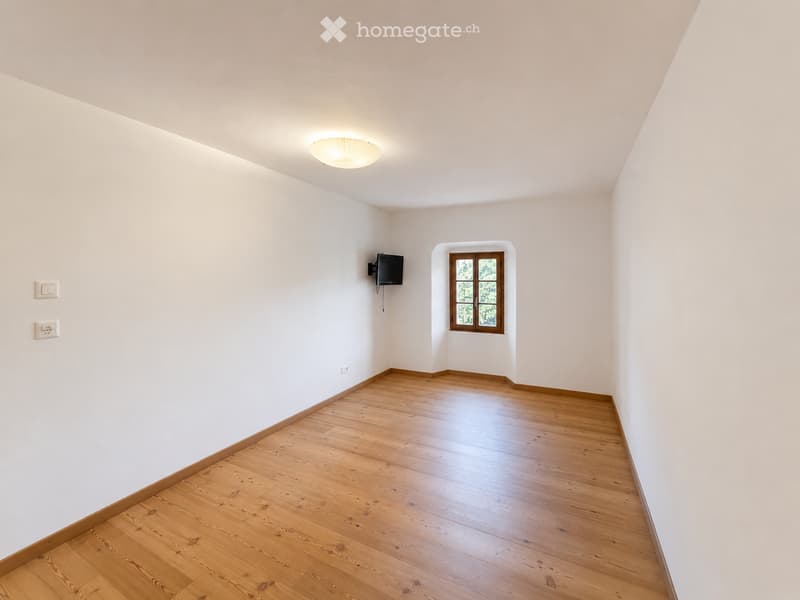 Empty room with wooden flooring, white walls, a single window, and a mounted TV on one wall.