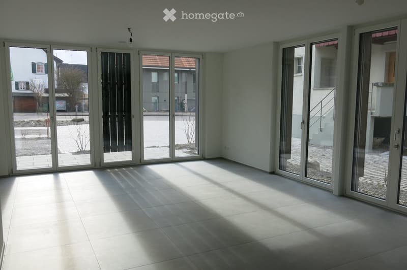 Empty room with sliding glass doors, white tiles, and a view of the outside.