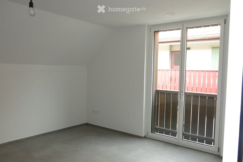 Empty room with white walls, tiled floor, and large sliding glass doors leading to a balcony with a pink railing.
