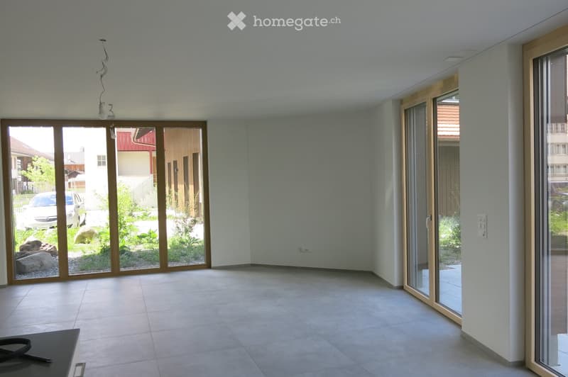 Empty room with large sliding glass doors leading to a garden, tiled floor, and white walls.