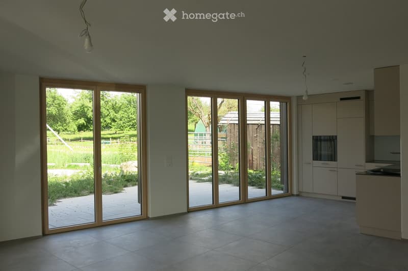 Bright, open room with large sliding glass doors leading to a garden, tiled floor, and modern cabinetry visible on one side.