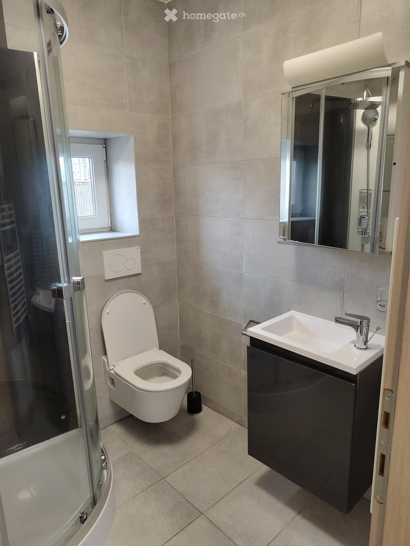 Modern bathroom with beige tiles, a white toilet, a black sink cabinet, a mirror, and a glass-enclosed shower area.