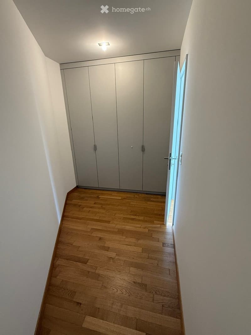 Empty hallway with wooden flooring, white walls, and built-in closet doors on one side.