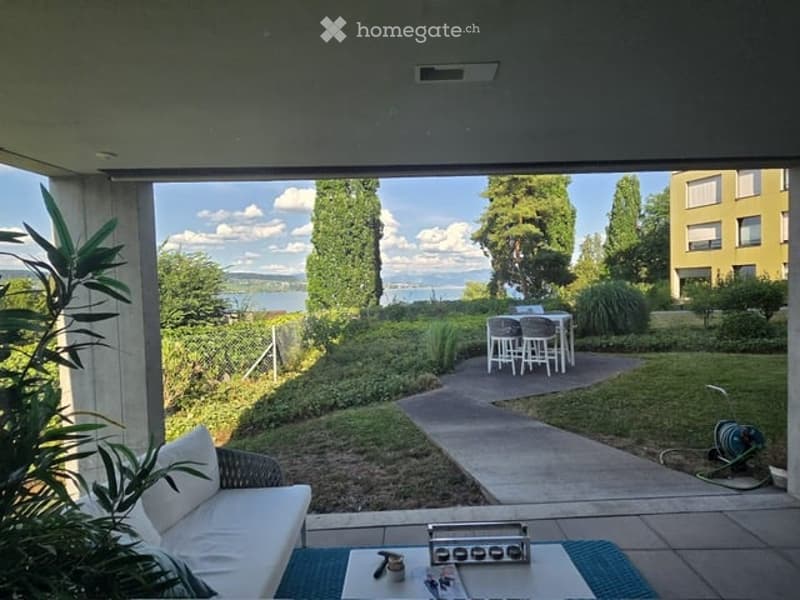 Balcony with a view of a lake, featuring a white sofa, a small table with chairs, and a blue rug.