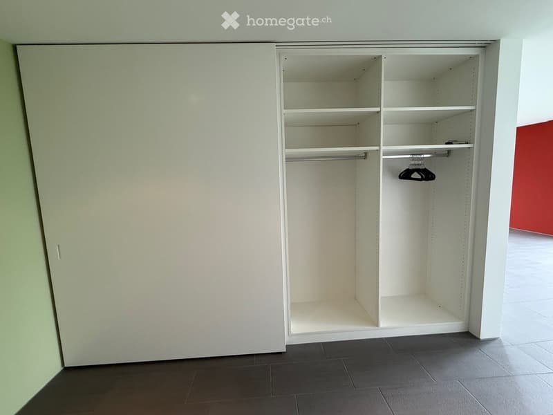 Empty room with a built-in closet featuring shelves and a hanging rod, dark tiled floor, and white walls.
