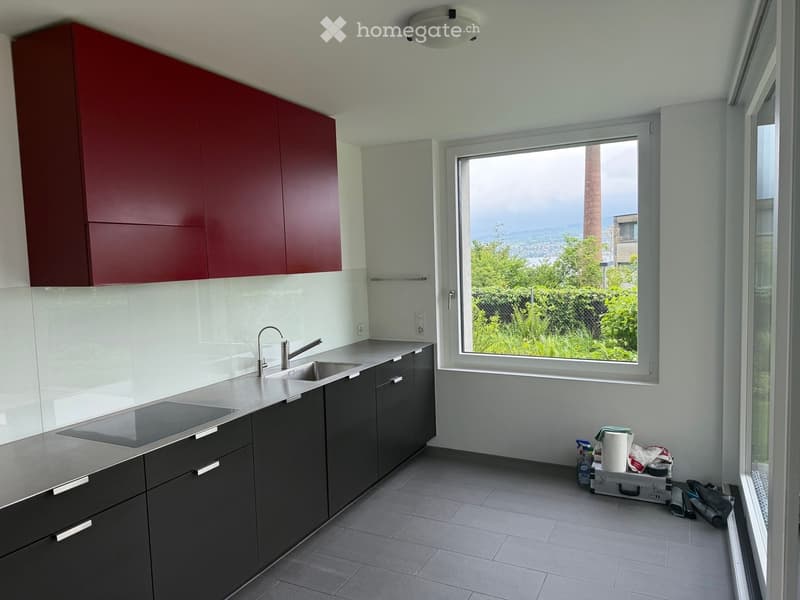 Modern kitchen with dark grey cabinets, a stainless steel sink, and a large window offering a view of greenery.