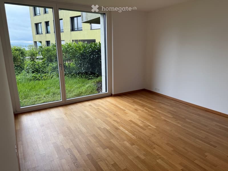Empty room with light wooden flooring and large sliding glass doors leading to a green outdoor area.