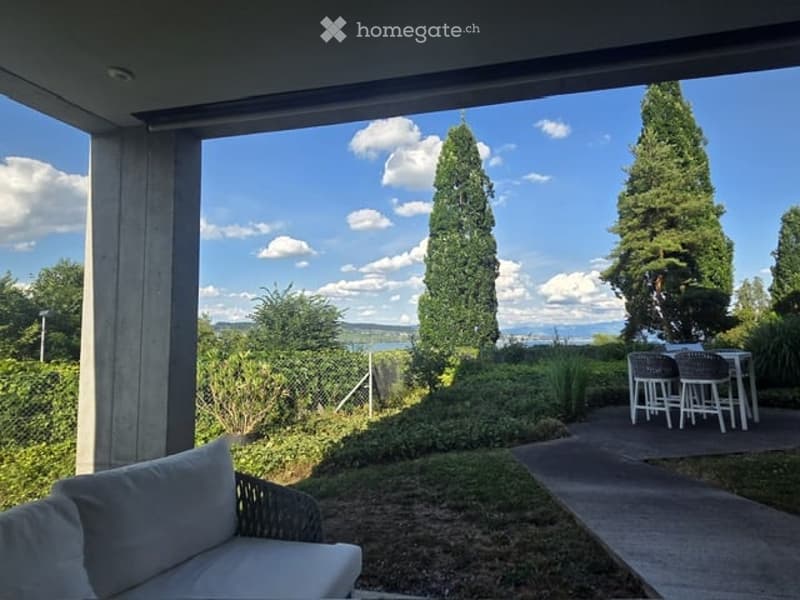 Balcony with outdoor seating area, overlooking a scenic view of trees and a body of water.