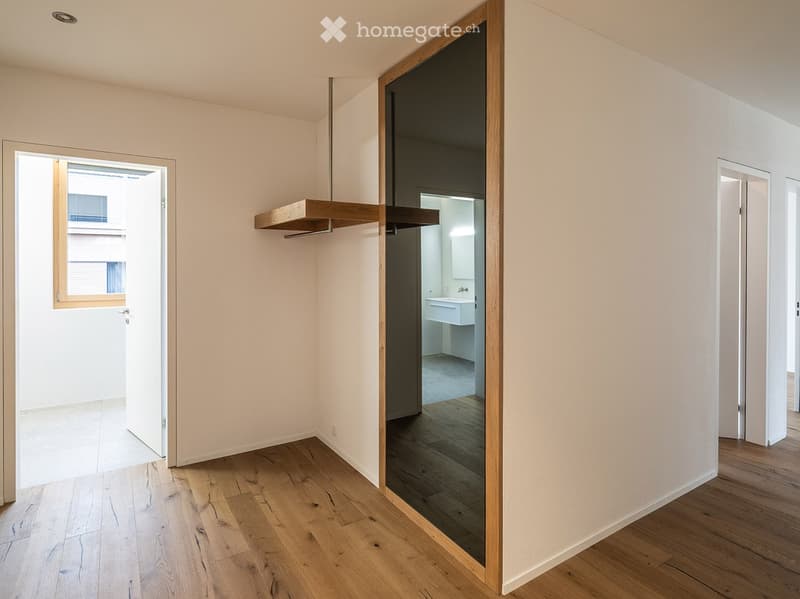 Empty room, wooden floor, mirror, doors on both sides, open door to another room, window on left