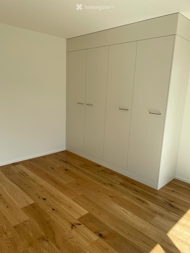 Empty room with light-colored wooden flooring and white built-in wardrobes.
