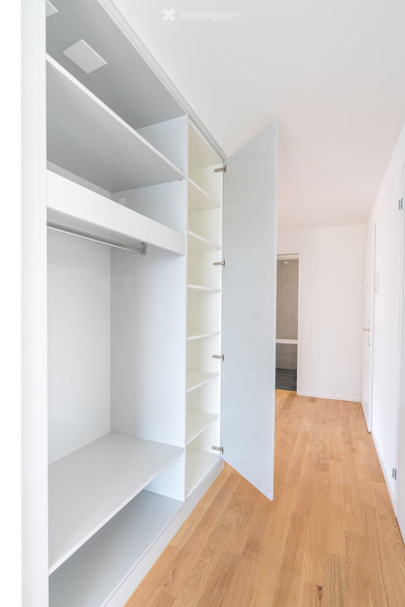 Empty room with white built-in closet and wooden flooring. The closet has multiple open shelves and a hanging rod, but no items are present.