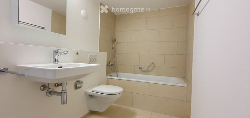 Modern bathroom with a white sink, toilet, bathtub, and showerhead. Beige tiled walls and floor, with a large mirror above the sink.