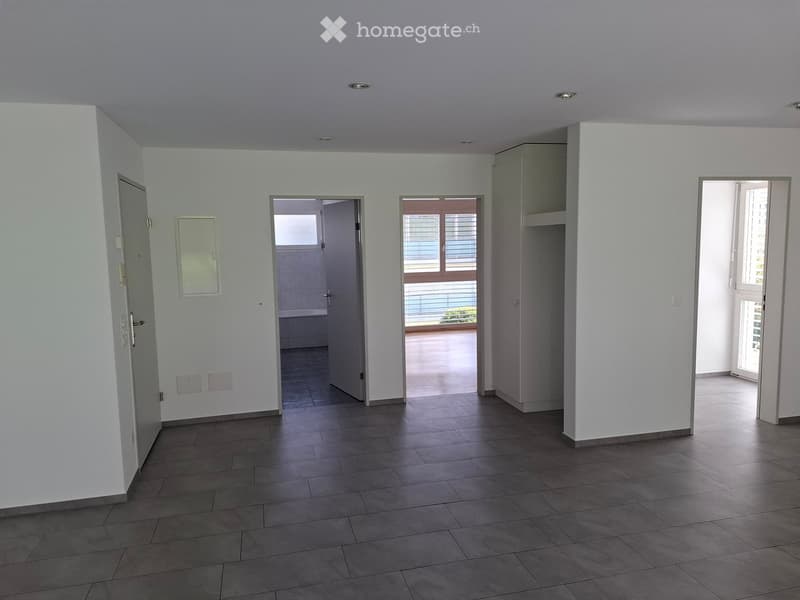 Empty hallway with tiled floor, white walls, and several doors leading to different rooms, including a bathroom and a balcony.