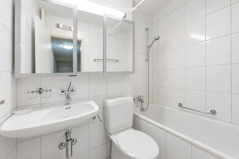 Modern bathroom with white tiles, a sink, toilet, bathtub, and a large mirror with built-in lighting.