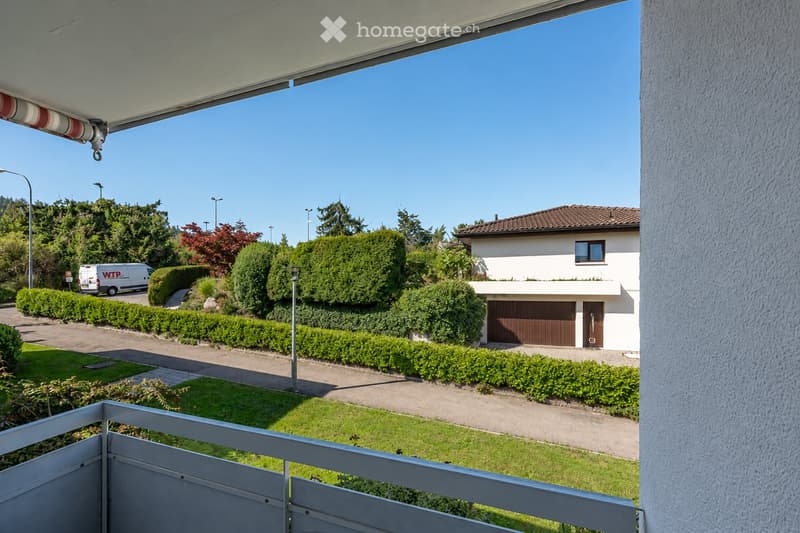 View from a balcony of a two-story house with a garage, surrounded by well-maintained hedges and a driveway.
