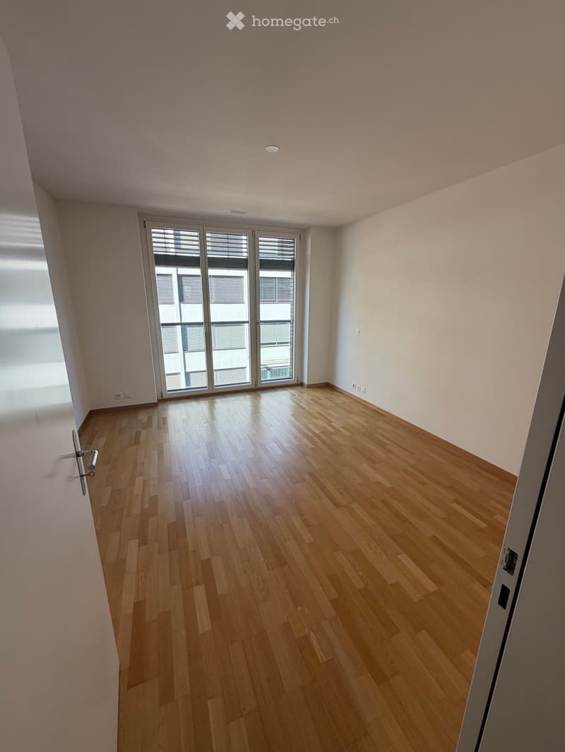 Empty room with light wooden flooring, white walls, and large glass sliding doors leading to a balcony.