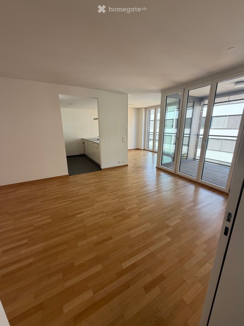 Empty room with light wooden flooring, white walls, and large sliding glass doors leading to a balcony area. The room is unfurnished and has a clean, minimalist design.