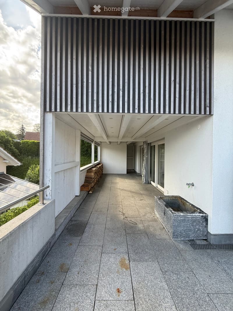 Modern balcony with tiled floor, white walls, metal railing, and a stone basin on the right side.