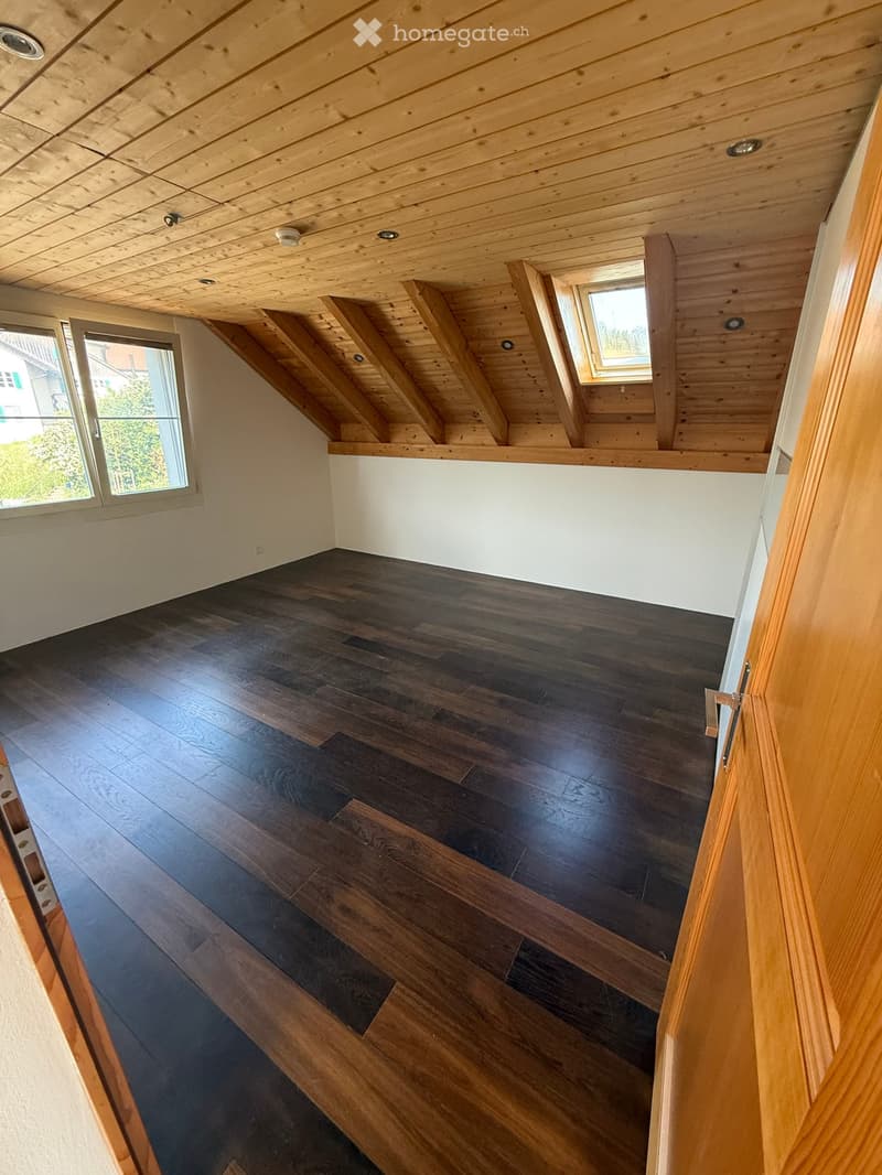 Empty attic space with wooden slatted ceiling, dark hardwood flooring, and skylight windows.