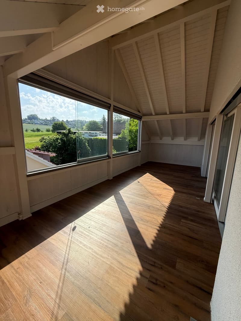 Empty attic room with wooden flooring, large windows, and exposed wooden beams on the ceiling.