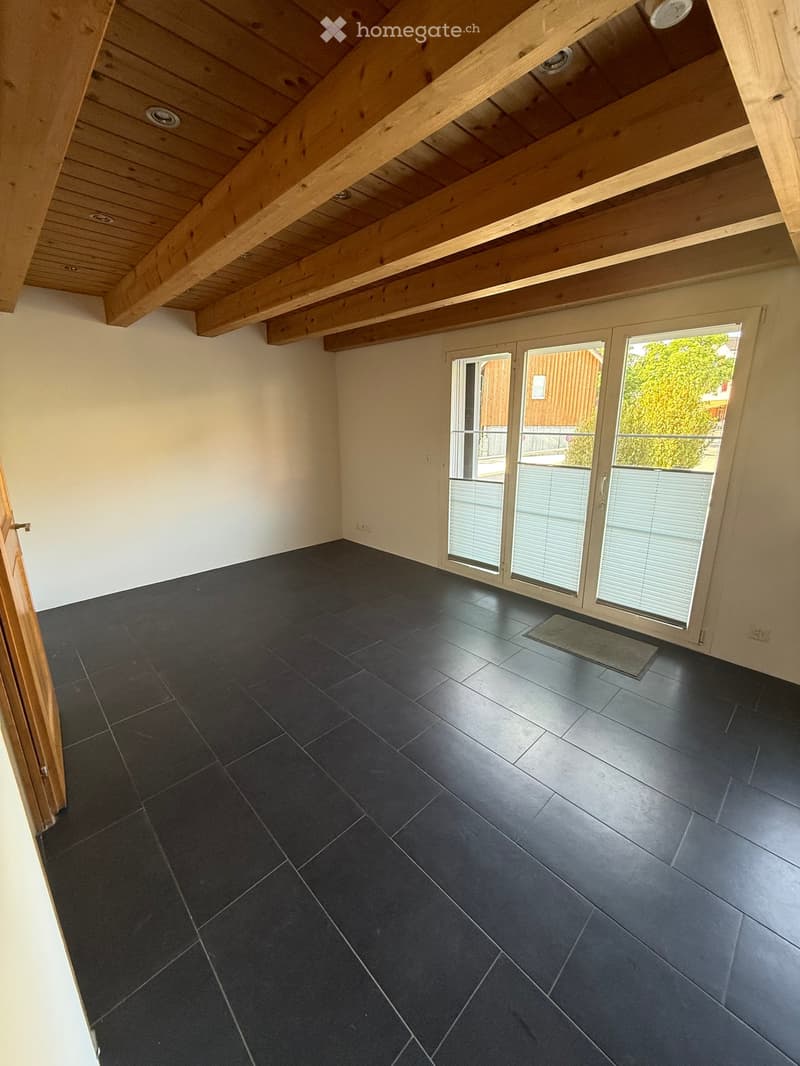 Empty room with dark tiled floor, white walls, wooden ceiling beams, and large sliding glass doors leading to a balcony.