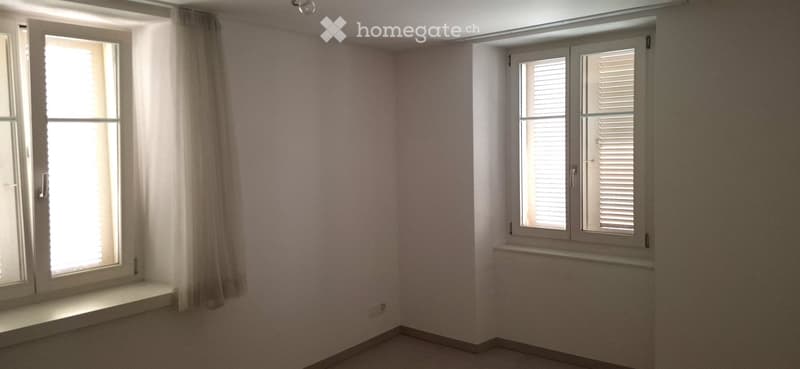 Empty room with light pink walls, white-framed windows, and a white curtain on one side.