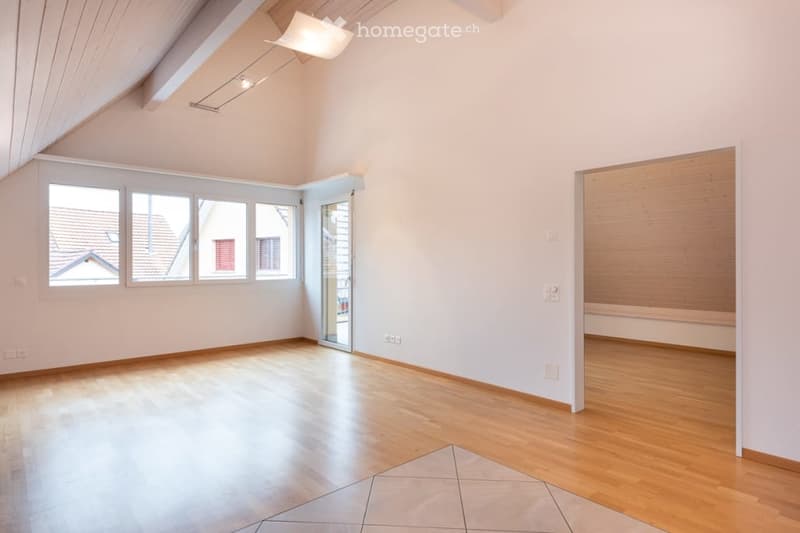 Bright, empty room with wooden flooring, white walls, large windows, and a sliding glass door leading to a balcony.