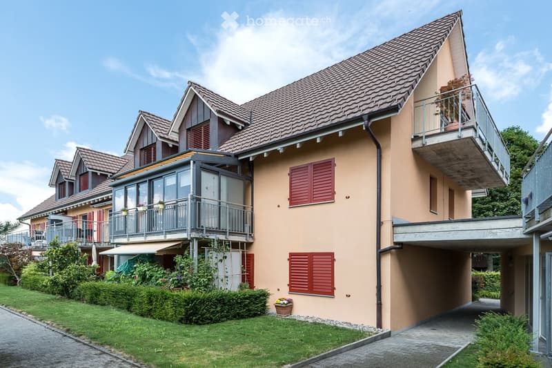 Two-story house with beige exterior, red shutters, multiple balconies, and a well-maintained garden.