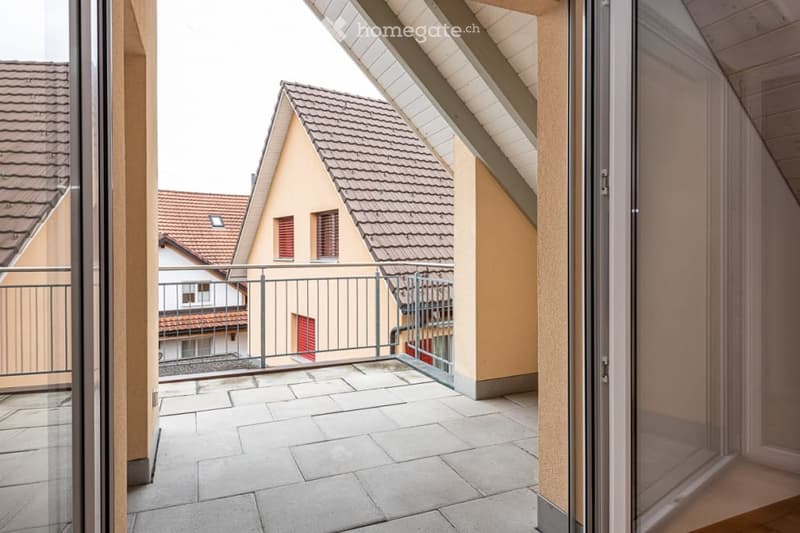 Balcony with tiled floor, metal railing, and view of neighboring houses with red-tiled roofs.