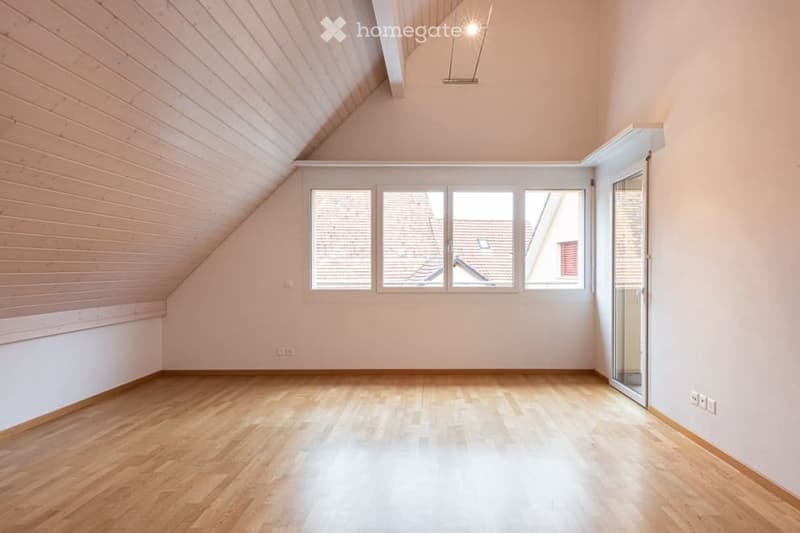 Empty attic room with wooden floors, white walls, large windows, and a skylight. No furniture or equipment present.