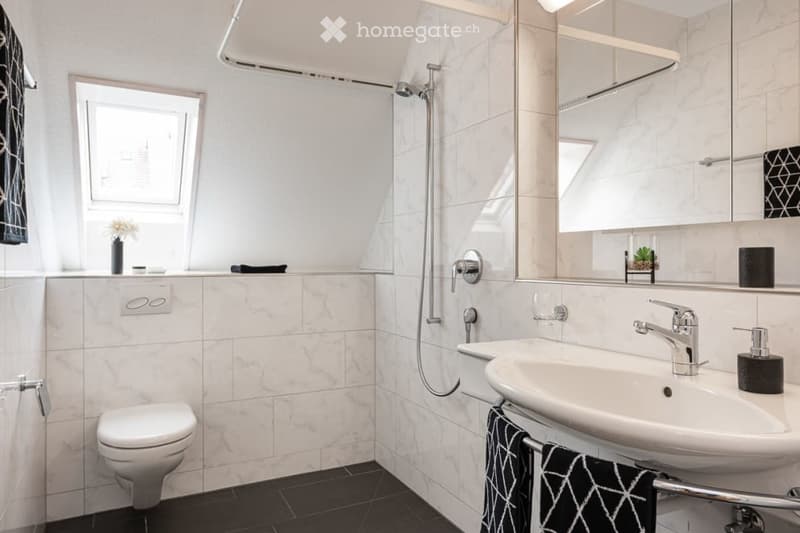 Modern bathroom with white marble tiles, a toilet, a sink with a modern faucet, a shower with a glass enclosure, a large mirror, and a towel hanging on a rack.