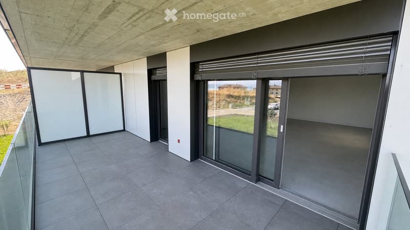 Modern balcony with large glass sliding doors, tiled floor, and a view of the surrounding landscape.