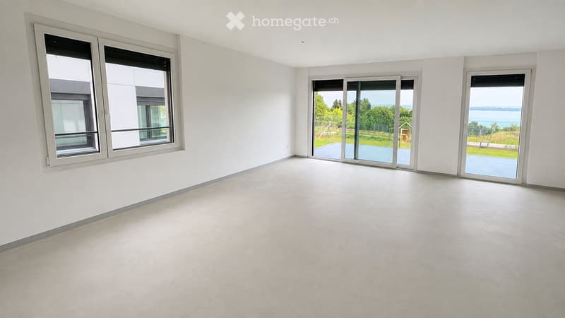 Empty room with white walls, large windows, and sliding glass doors leading to a patio area.