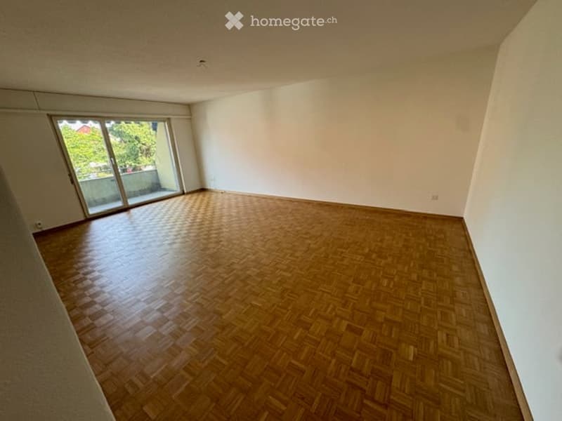 Empty room with wooden parquet flooring, white walls, and large sliding glass door leading to a balcony.