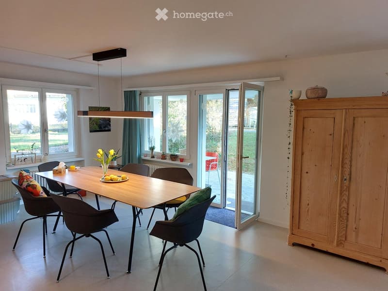 Bright dining area with a wooden table, six chairs, a large window, and a sliding glass door leading to a patio.