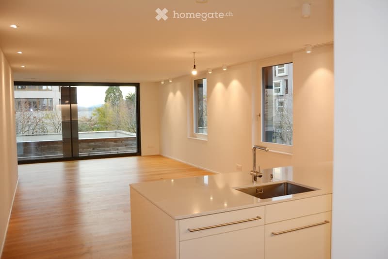 Modern kitchen with white cabinets, a central island, and a stainless steel sink. Large windows offer a scenic view of the outdoors.