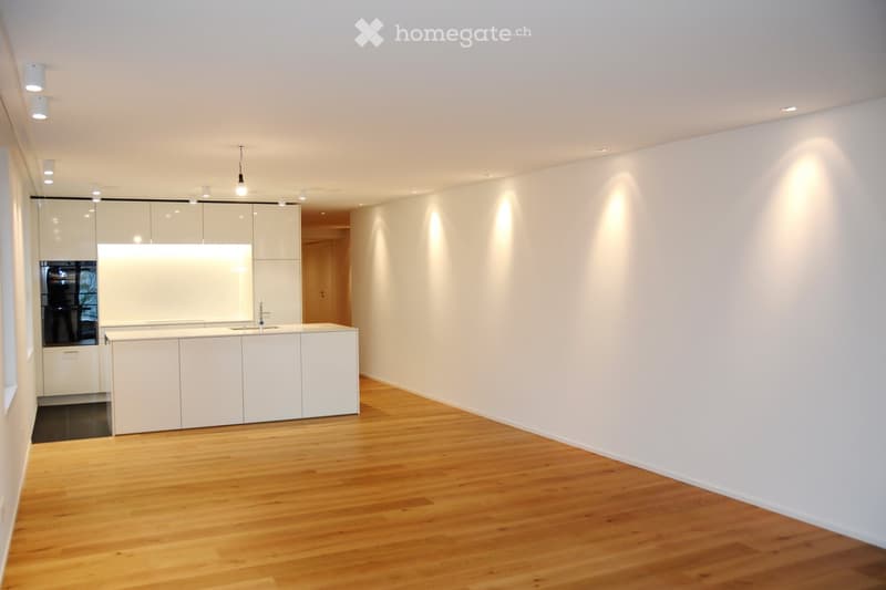 Modern, minimalist kitchen with white cabinets, a central island, and a sleek sink. The space features wooden flooring and recessed lighting.
