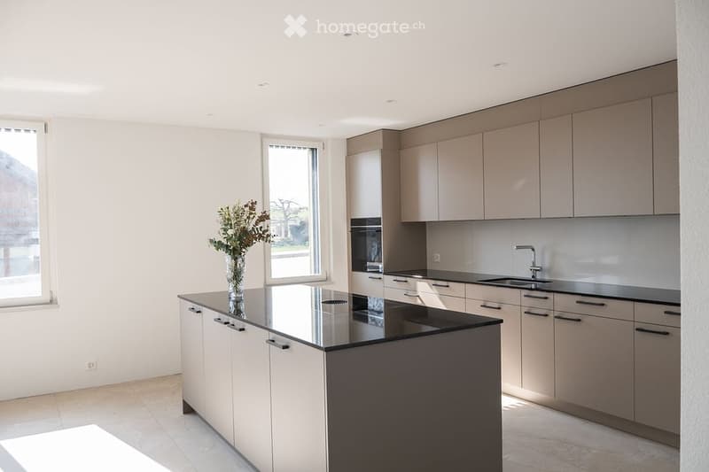 Modern kitchen with light-colored cabinetry, a black countertop island, and a vase with flowers on the island. The kitchen features a sink, faucet, and large windows offering a view of the outdoors.