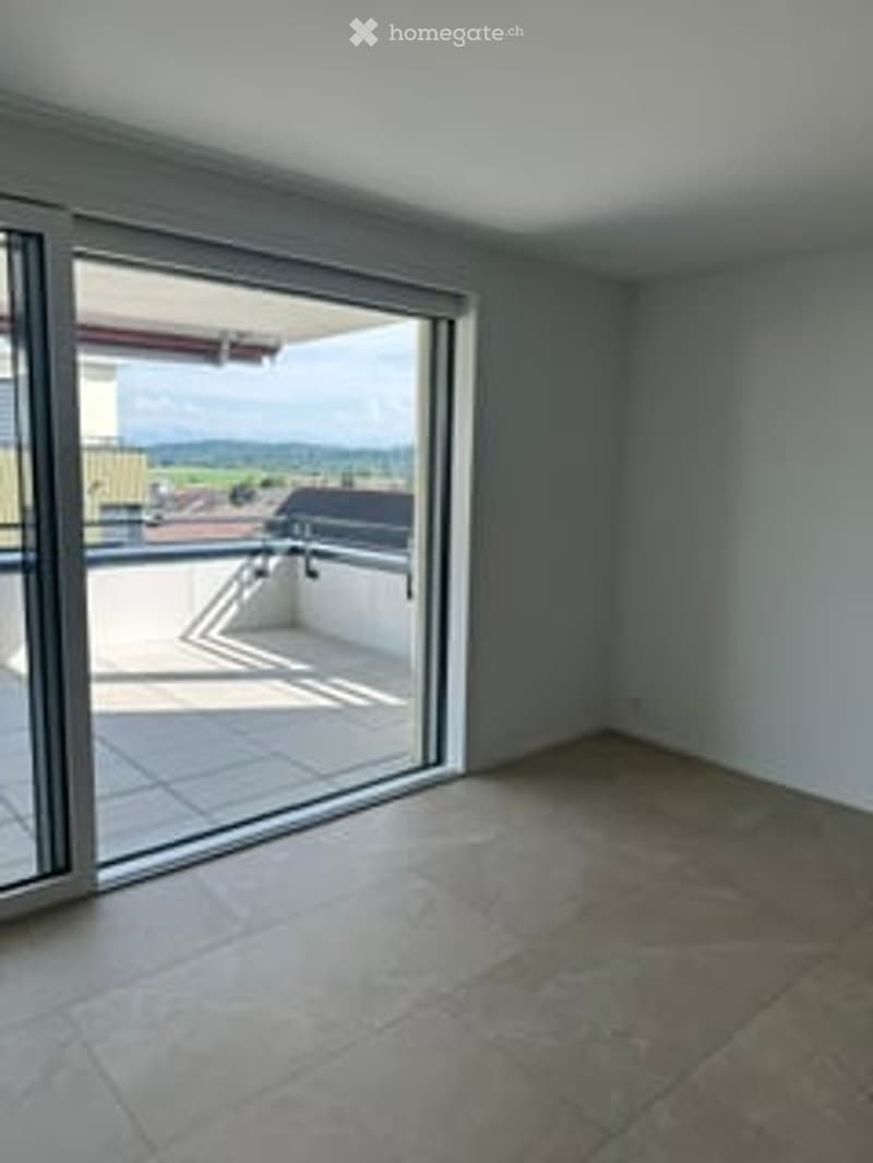 Empty room with large sliding glass doors leading to a balcony or terrace area. The floor is tiled, and the walls are painted a neutral gray.