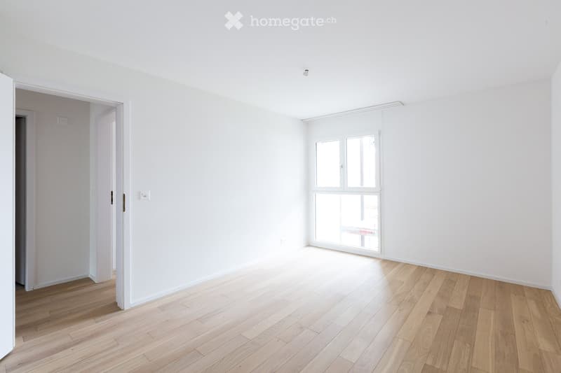 Empty room with white walls, wooden flooring, and large windows allowing natural light. No furniture or personal items are present.