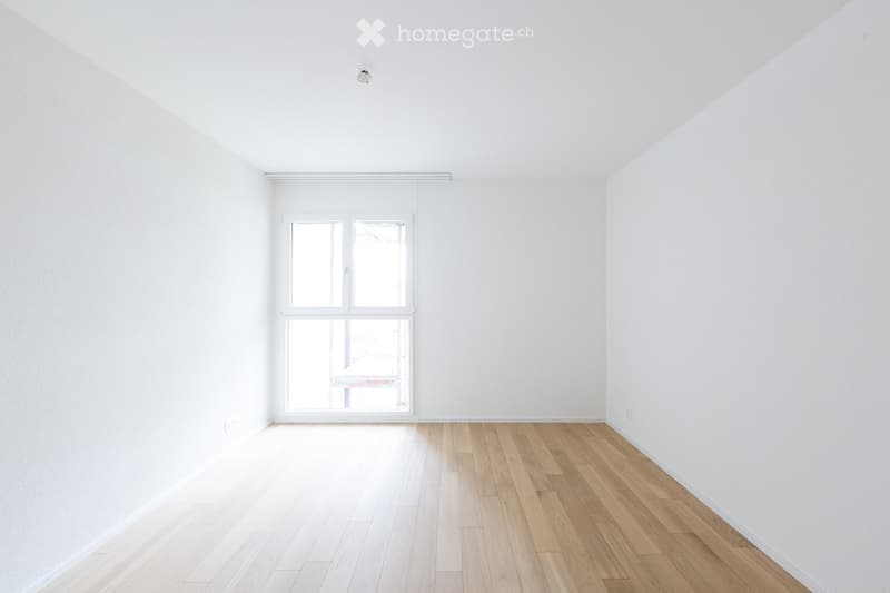 Empty room with white walls, wooden floor, and large window with white frame. No furniture or equipment visible.