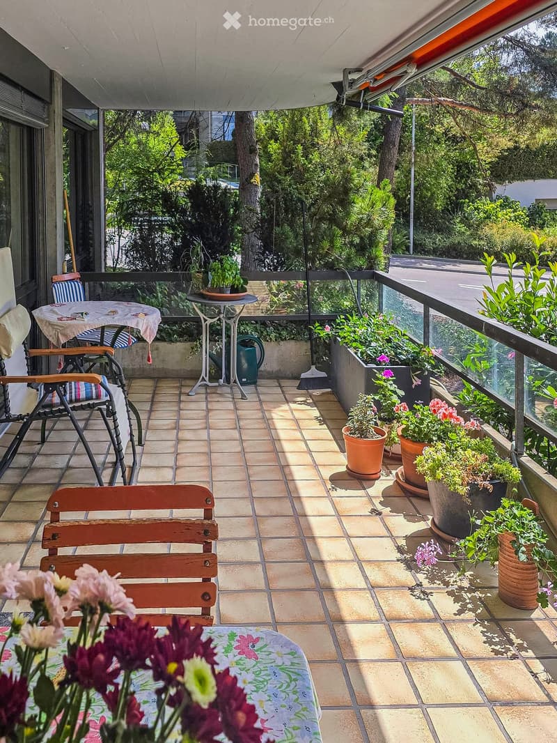 Balcony with tiled floor, wooden chair, small table, potted plants, and an umbrella.