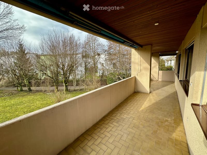 Balcony with tiled floor, wooden ceiling, and a view of a grassy area with trees.