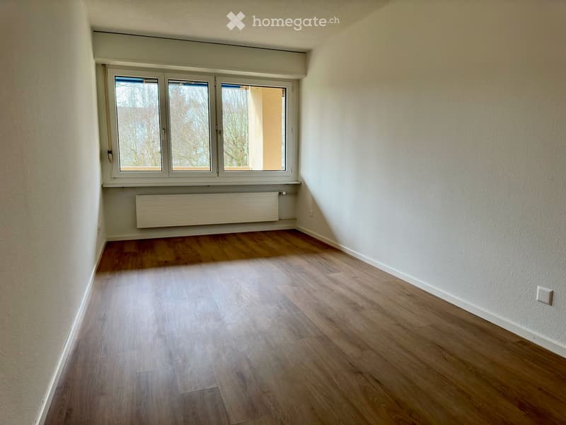 Empty room with wooden flooring, white walls, and a large window with a radiator below it.