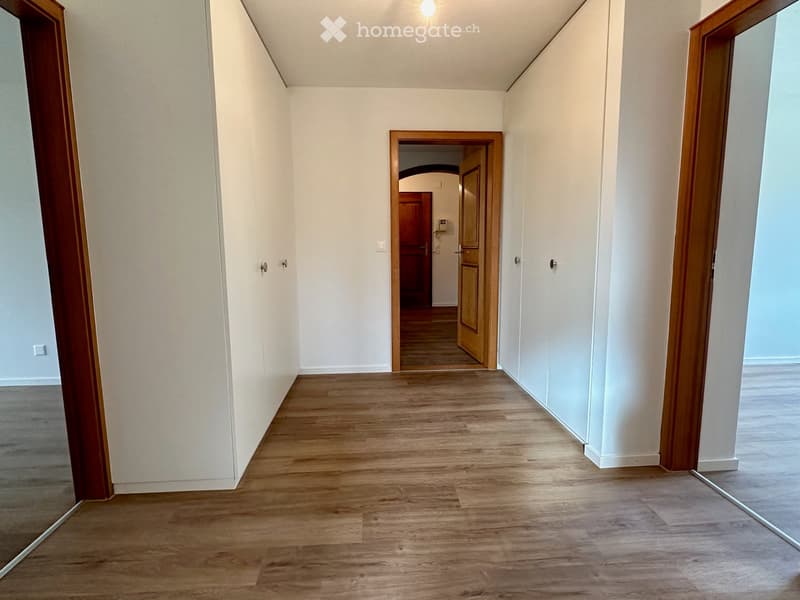 Empty hallway with wooden flooring, white walls, and several doors leading to other rooms.
