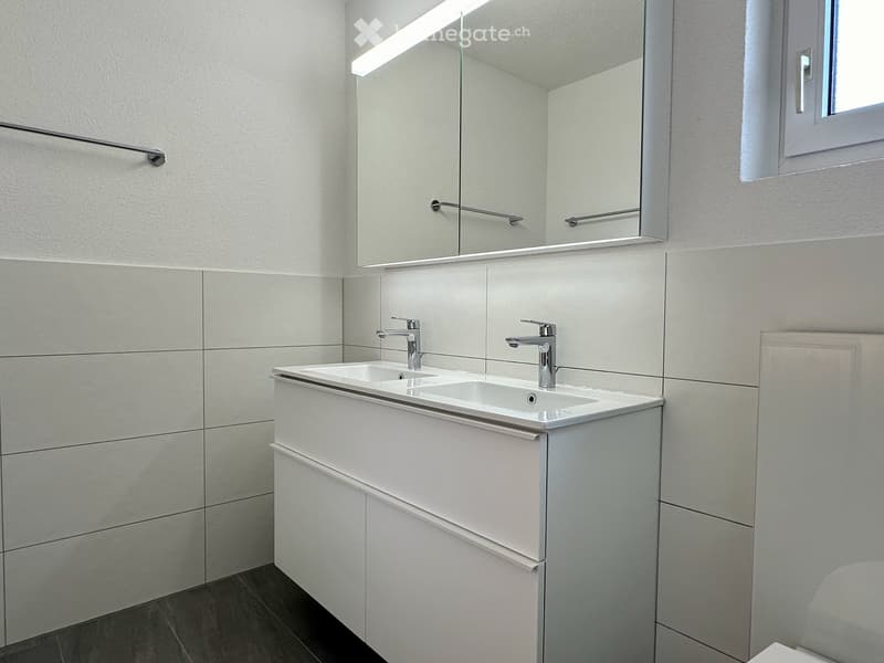 Modern bathroom with a double sink, sleek white cabinetry, and a large mirror above the sink.