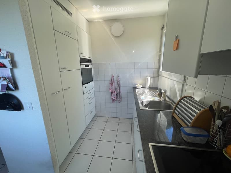 Modern kitchen with white cabinets, tiled walls and floor, stainless steel sink, microwave, and various kitchen utensils.
