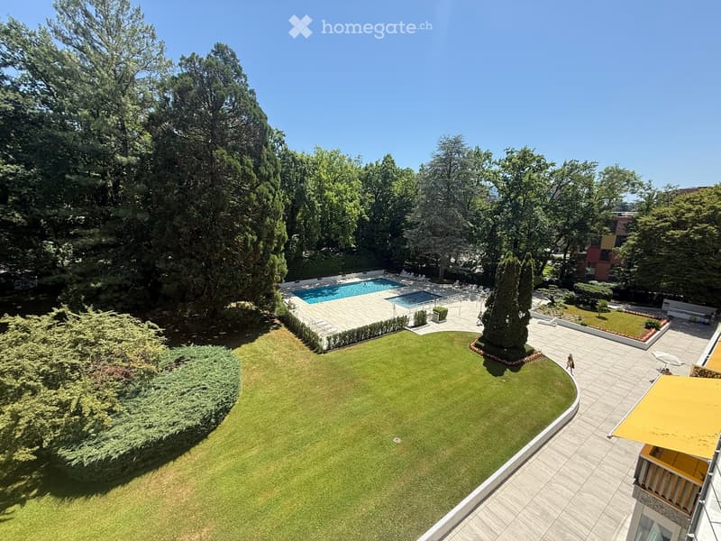 Aerial view of a well-maintained garden area with a large lawn, a swimming pool, lounge chairs, and surrounding trees.