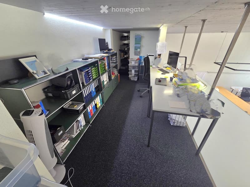 Office space with a desk, chairs, computer, screen, fan, shelves, filing cabinet, and a mirror on the wall.